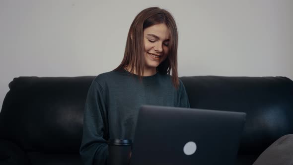 The Cheerful Student with Red Hair and a Wide Smile Types a Message to Her Colleagues on Her Laptop