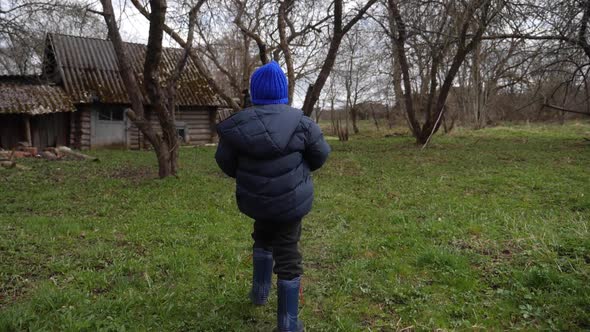 Boy Child in a Blue Hat Walks Through the Yard