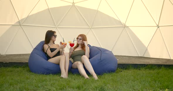 Two Girls in Swimsuits with Cocktails Resting on Bg Chairs