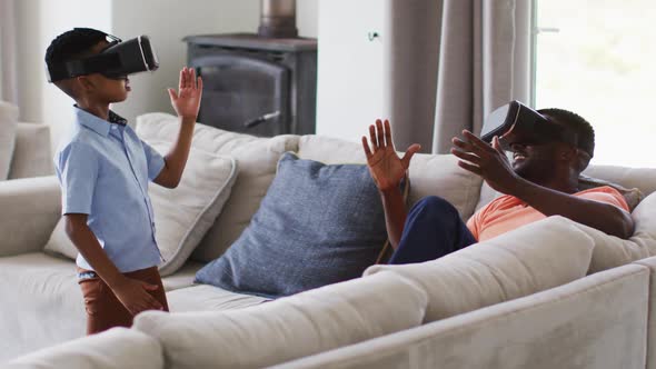 African american father and son using vr headsets together on a couch