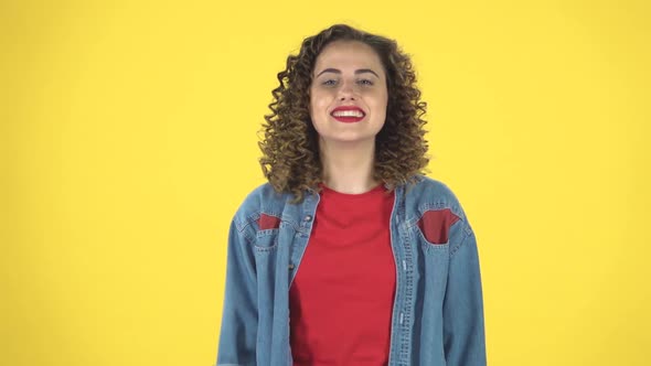 Young Curly Girl Shows Two Fingers Victory Gesture on Yellow Background at Studio, Slow Motion