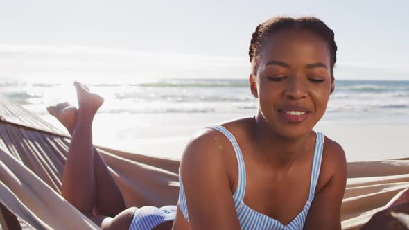 African american woman using digital tablet while lying on a hammock at the beach