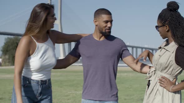 Two Female Friends Kissing African American Man on Meadow.