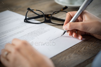 iting on a financial contract. Shallow depth of field with focus on tip of the pen.