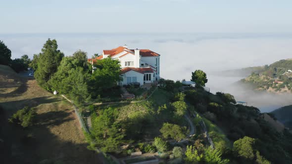 Scenic Aerial Shot of Home on Top of the Green Mountain and Clouds at Sunrise