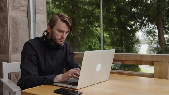 A Creative Programmer in Headphones Sits at a Table and Analyzes Statistics on a Laptop