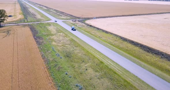 Vehicles Driving By The Rural Road Between Wheat Fields - aerial drone shot