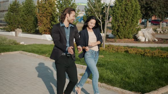 Joyful Couple Mixedrace Youth Walking and Clapping Hands Enjoying Warm Sunny Day in City