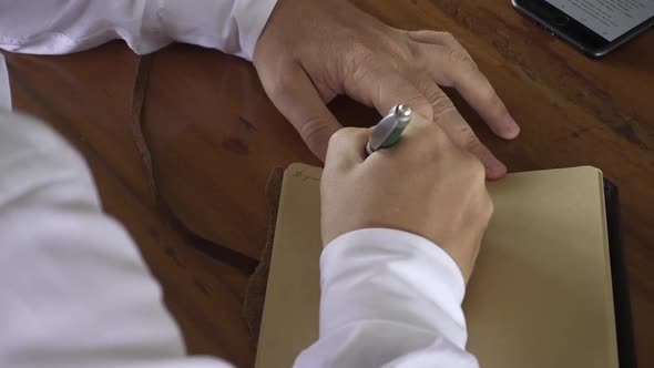 Groom's vow. Male  hands writing letter in vintage notebook on wooden table. Wedding accessories