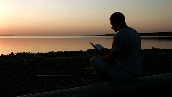 Man Reading a Book After Sunset on the Lake