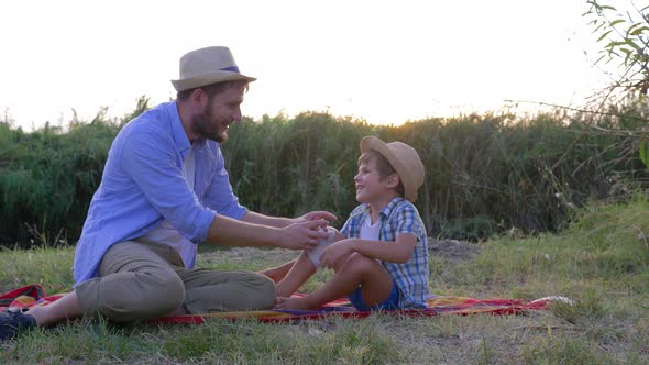 Daddy Putting Bandage on Injured Leg of Son Sitting on Plaid During a Family Weekend at Sunset