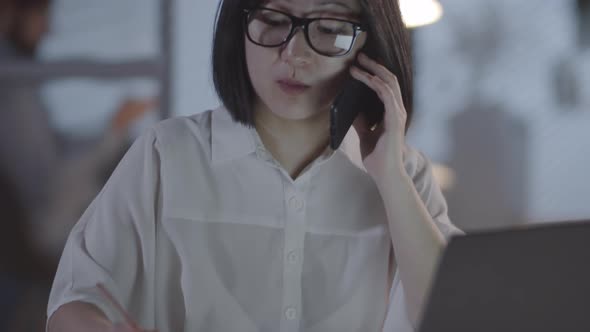 Asian Businesswoman Talking on Phone in Office in Evening