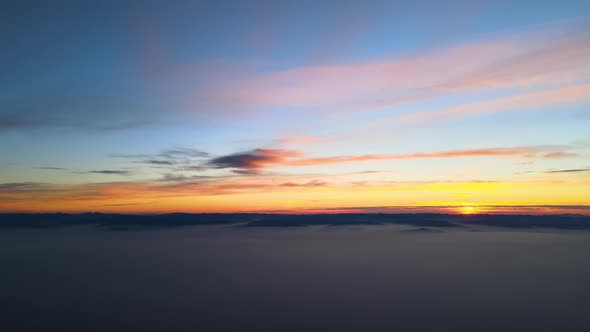 Aerial View of Colorful Sunset Over White Dense Foggy Clouds Cover with Distant Dark Silhouettes of