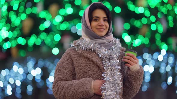 Smiling Beautiful Woman Looking at Camera Turning to Christmas Lights at Background