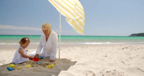 Little Girl Playing At The Beach Sand With Mom