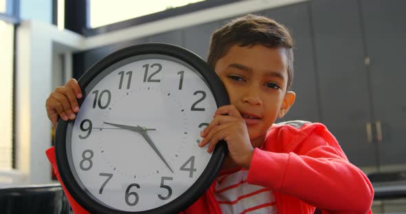 Front view of Asian schoolboy holding wall clock at desk in classroom at school 4k