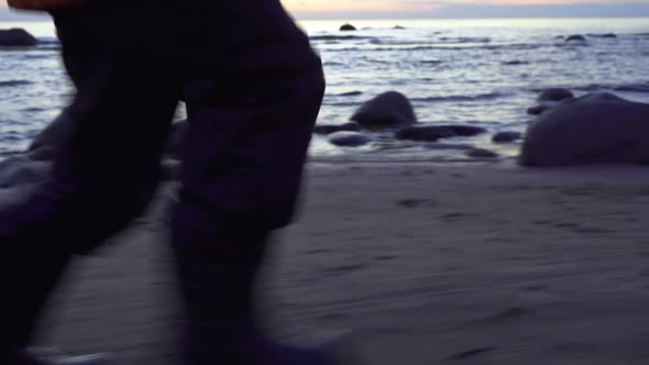 a Child in Boots and a Jacket Runs Along the Shore of the Bay