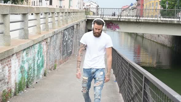 slow motion young beautiful bearded man outdoor listening music walking down the street