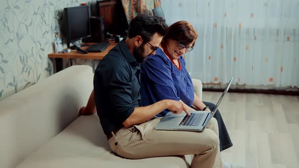 Family Relationship Online Chatting Social Network. Parent Mother And Adult Grown Son Sit On Sofa.