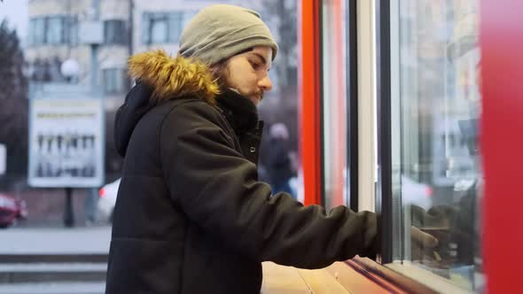 A man pays for coffee with his phone at a kiosk in daylight. Side view