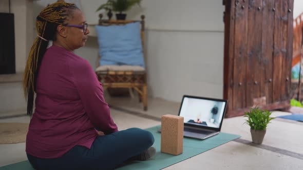 African senior woman doing yoga virtual fitness class with laptop at home