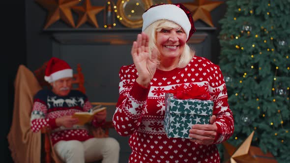 Mature Grandmother in Christmas Sweater Smiling Friendly at Camera and Waving Hands Gesturing Hello