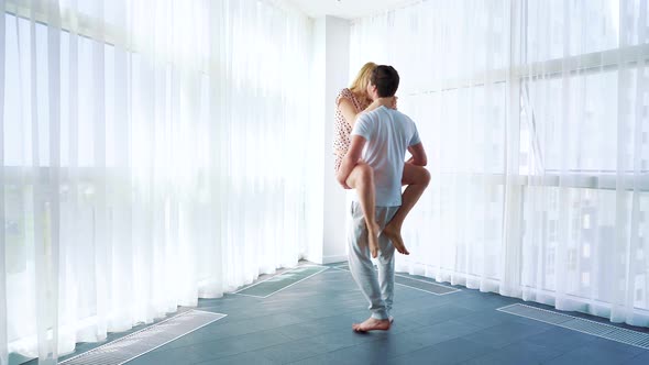 Young Man Holds Woman in his Arms and Spins Around in Spacious Room