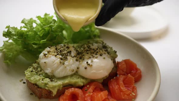 Chef Pours Sauce on Toast with Guacamole and Poached Eggs