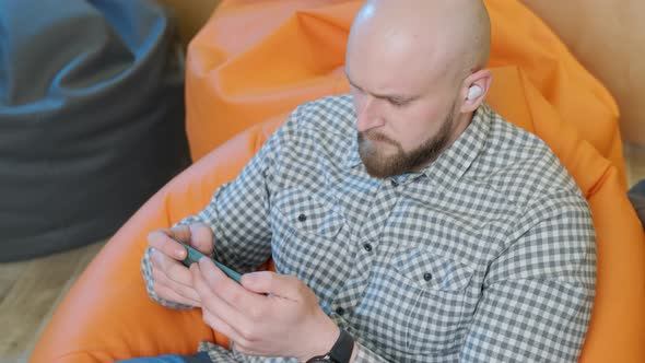 Young Man Sits on a Bean Bag While Playing Online Using His Phone