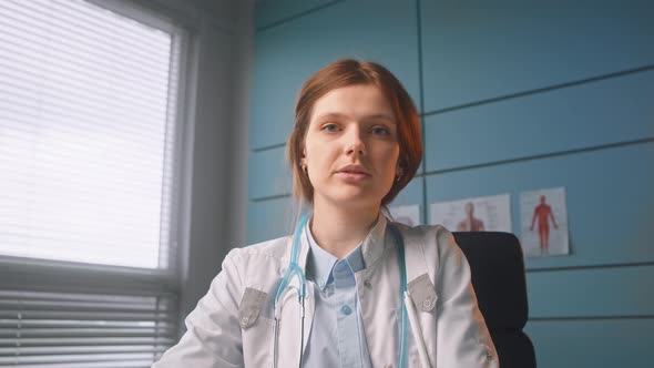 Serious lady doctor in white coat talks to patient at online meeting