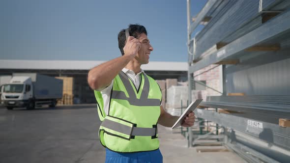 Portrait of Happy Positive Middle Eastern Expert Inspector in Headphones Walking at Warehouse