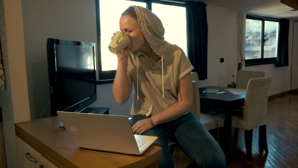 Woman At Home Chatting On Laptop And Drinking Tea