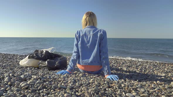 a woman in a denim suit is sitting on the seashore after garbage collection,
