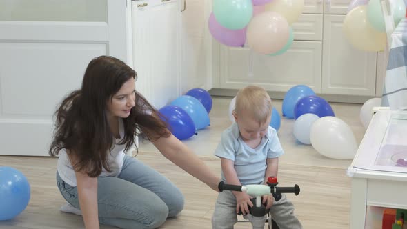 Mother and Baby Boy Play on the Floor Mother Teaches 1 Year Old Child to Ride a Balance Bike