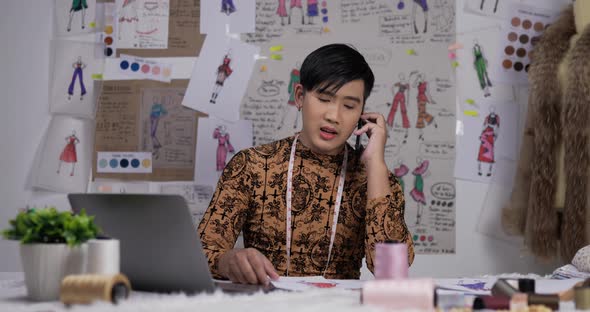 Angry Asian clothing designer talking on mobile in his office