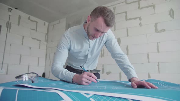Young engineer-architect in a bright room works with blueprints laid out on a table