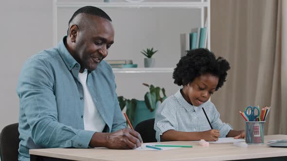Mature African American Father with Little Kid Girl Sitting in Room at Desk Draws Colored Pencils