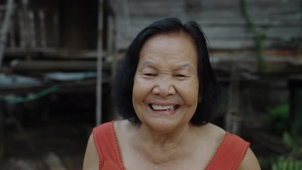 Thai elderly woman in round-necked sleeveless collar laughing in old wooden home