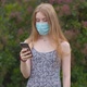 A young girl in a protective medical mask looks at the phone and sends messages - VideoHive Item for Sale