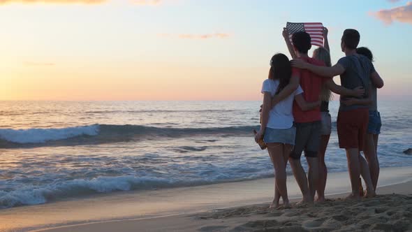 Group of friends holding american flag on the beach 