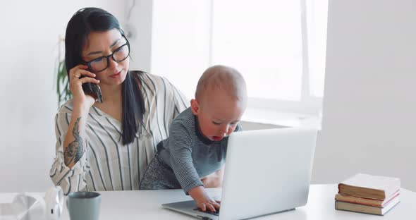 Young Mother Freelancer with Her Child Working at Home Office Using Laptop