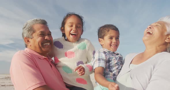 Happy hispanic grandparents and grandchildren having fun on beach at sunset