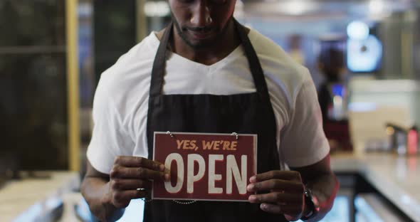 Portrait of happy african american barista holding 'we're open' sign in cafe