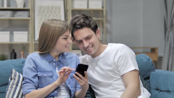 Happy Young Couple Browsing Internet on Smartphone at Home