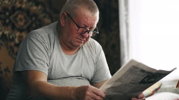 A Mature Man in Glasses Reading a Newspaper at Home