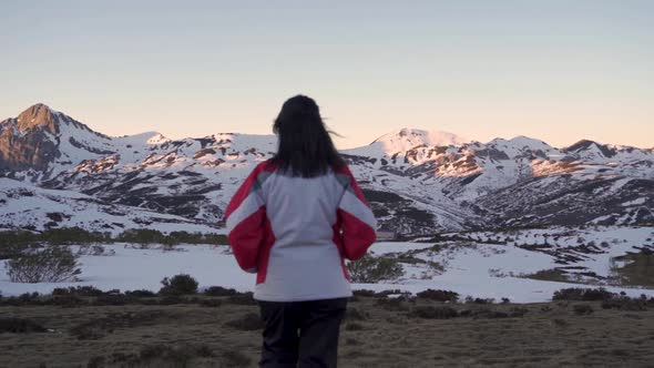 Women in a winter clothing walking towards snow covered mountains at dusk
