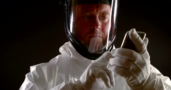 a Man Is Dressed in White Protective Clothing, a Mask with a Transparent Visor and Gloves. He Holds