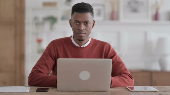 African Man Smiling at Camera while using Laptop in Office