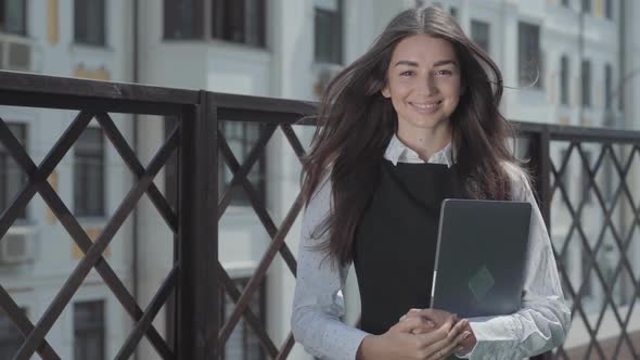 Portrait of a Pretty Young Woman on the Terrace Looking in the Camera Holding Laptop in Hands