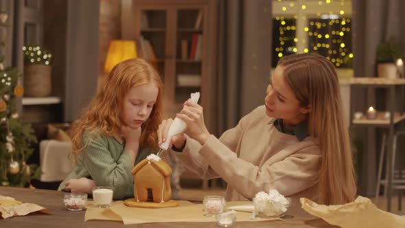 Woman Decorating Gingerbread House With Daughter